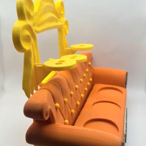 May include: An orange miniature sofa with a yellow decorative top and two yellow side tables. The sofa has a tufted back with yellow button details. The design is reminiscent of the iconic couch from the TV show "Friends".