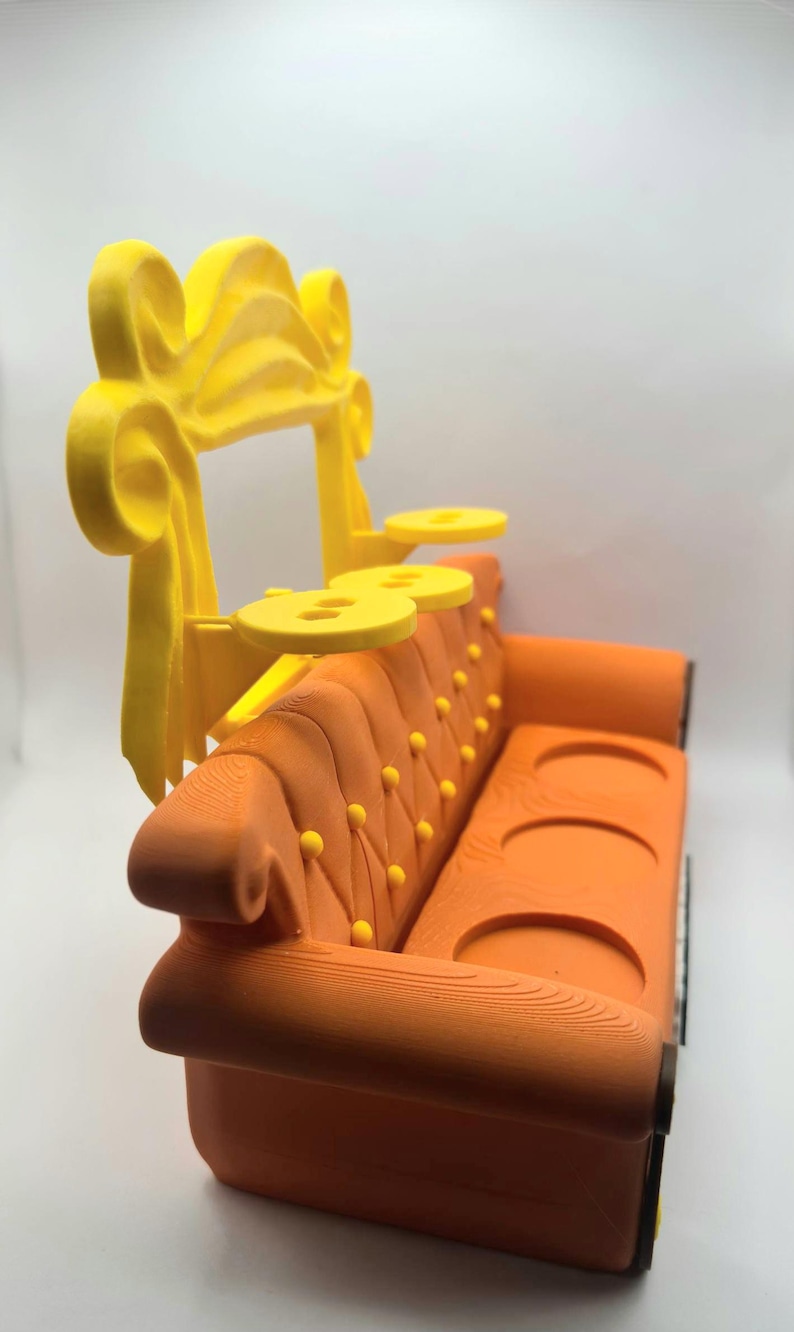May include: An orange miniature sofa with a yellow decorative top and two yellow side tables. The sofa has a tufted back with yellow button details. The design is reminiscent of the iconic couch from the TV show "Friends".