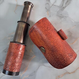 May include: A vintage brass telescope with a wooden case. The telescope is extended and has a dark finish. The wooden case is brown with engraved details and the word "LONDON" is visible.