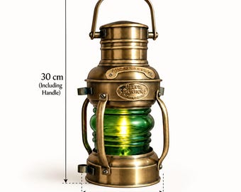 Op de afbeelding: Een nautische lantaarn van messing met een groen glazen middenstuk, voorzien van een handvat aan de bovenkant en een metalen plaatje met de tekst "DEEDS BURTON". De lantaarn is 30 cm hoog inclusief handvat en heeft een diameter van 12,5 cm.