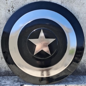 Puede incluir: Un escudo negro y plateado con un emblema central de estrella plateada. El escudo tiene un dise&ntilde;o circular con anillos conc&eacute;ntricos negros y plateados. La estrella es un dise&ntilde;o de cinco puntas con acabado met&aacute;lico.