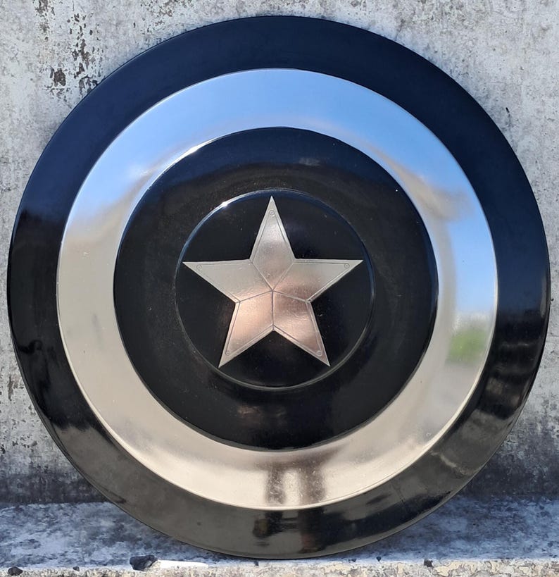 Puede incluir: Un escudo negro y plateado con un emblema central de estrella plateada. El escudo tiene un dise&ntilde;o circular con anillos conc&eacute;ntricos negros y plateados. La estrella es un dise&ntilde;o de cinco puntas con acabado met&aacute;lico.