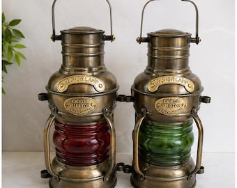 May include: Two antique-style brass anchor lamps with top handles. One lamp features a red glass lens, and the other features a green glass lens. Each lamp has a brass plate embossed with the text ANCHOR LAMP and LEEDS BURTON SOUTHAMPTON.