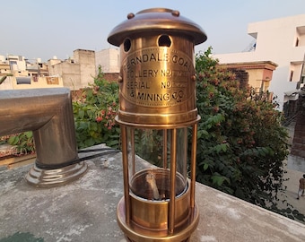 Op de afbeelding: Een antieke messing mijnwerkerslamp met een glazen cilinder en de tekst "Ferndale Coal Colliery No. 374 Serial No. 2071 & Mining Co." De lamp heeft een gewelfde bovenkant en een ronde basis. Het is een vintage item.