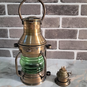 Peut inclure: Une lanterne antique en laiton avec une section centrale en verre vert et une poignée. Une petite lampe à huile en laiton est à côté. Le fond est un mur de briques.
