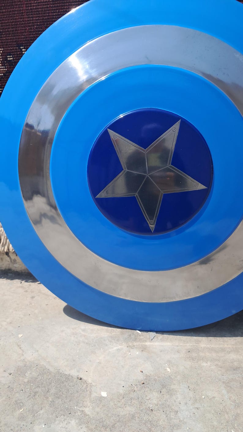 Op de afbeelding: Een blauw en zilver schild met een centraal sterontwerp. Het schild heeft concentrische cirkels van blauw en zilver, met een donkerblauw centrum met een zilveren ster. Een klassiek superheldenaccessoire.