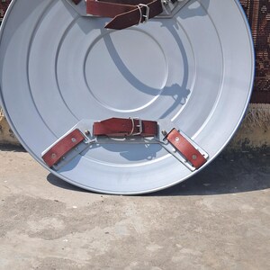 Op de afbeelding: Een zilverkleurig, rond schild met concentrische cirkels. Het schild heeft vier bruine leren riemen met zilveren gespen en klinknagels om het vast te zetten. Het schild is waarschijnlijk van metaal. Diameter ongeveer 76 cm.