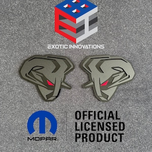 Pode incluir: Dois emblemas de metal cinza com detalhes vermelhos, apresentando um design estilizado de cabeça de carneiro. A imagem inclui o texto "EXOTIC INNOVATIONS", o logotipo da Mopar e o texto "OFFICIAL LICENSED PRODUCT".