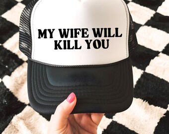 Peut inclure: Casquette de camionneur noire et blanche avec le texte "MY WIFE WILL KILL YOU" en noir. La casquette a un panneau avant blanc, une visière noire et un dos en filet noir. La casquette est tenue par une personne.