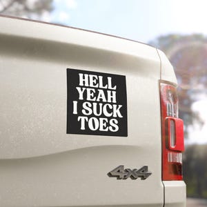 Puede incluir: Una pegatina cuadrada negra con texto blanco que dice HELL YEAH I SUCK TOES en una fuente negrita y ondulada. La pegatina está aplicada en el portón trasero de color claro de un vehículo, cerca de la luz trasera roja y un emblema plateado 4x4.