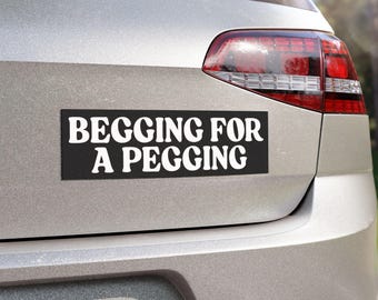 Può includere: Un adesivo rettangolare nero per paraurti con testo bianco che recita BEGGING FOR A PEGGING in un carattere grassetto senza grazie. L'adesivo è applicato sul bagagliaio argentato di un veicolo, posizionato orizzontalmente sotto il lunotto posteriore.