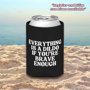 May include: A black foam can cooler featuring the white text "EVERYTHING IS A DILDO IF YOU'RE BRAVE ENOUGH" printed on the front. The top of a silver aluminum beverage can is visible. Text at the top reads "Regular and Slim can sizes available".