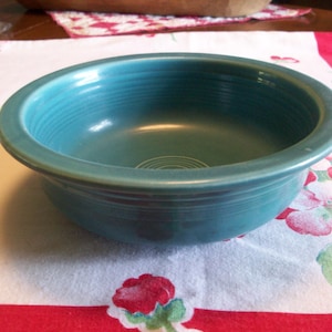 May include: A teal blue ceramic bowl with a smooth, rounded rim. The bowl has a subtle, rippled pattern on the inside.