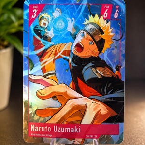 May include: A rectangular trading card featuring Naruto Uzumaki with spiky blonde hair and a blue and orange outfit. The card displays the text Naruto Uzumaki, Wind/Hidden Leaf Village, DMG 3, POW 6, and HP 6. The artwork shows a dynamic action pose.