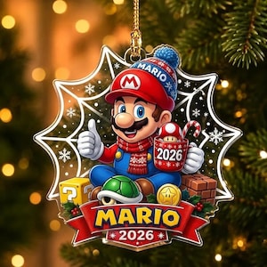 May include: A star-shaped Christmas ornament featuring Mario wearing a red hat and blue overalls, giving a thumbs up. He holds a red mug labelled 2026 with a mushroom inside. Below him is a green shell, a yellow block, and a red banner reading MARIO 2026.