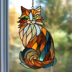 以下が含まれることがあります： オレンジ、茶色、青色のステンドグラスの猫のサンキャッチャー。猫は緑色の目をし、ふわふわの尻尾をしています。装飾品はチェーンから吊り下げられており、窓に飾るように設計されています。