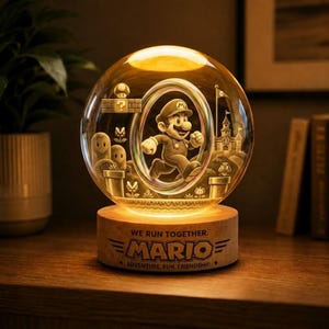 May include: A glowing, spherical lamp featuring a 3D depiction of Mario running through a level. The lamp has a wooden base with the text "WE RUN TOGETHER. MARIO" and is lit with a warm, yellow light. The scene includes iconic elements from the game.