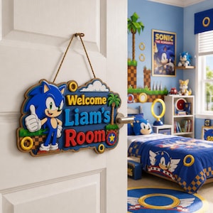 Könnte beinhalten: Ein hängendes Türschild aus Holz mit der blauen Figur Sonic the Hedgehog, die einen Daumen hoch zeigt. Das Schild hat einen blauen Hintergrund mit dem Text Welcome Liam's Room in gelber, hellblauer und roter Schrift, verziert mit goldenen Ringen.