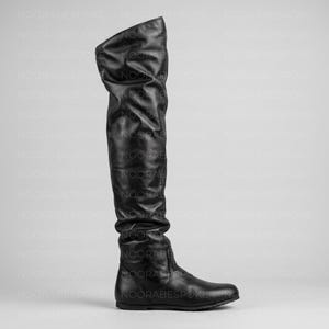 Puede incluir: Una bota negra por encima de la rodilla con un acabado liso y mate y un diseño de caña holgada. La bota presenta una puntera redondeada, una suela plana y una silueta limpia que se extiende por encima de la rodilla con pliegues verticales.