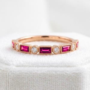 May include: A rose gold band ring featuring an alternating pattern of rectangular baguette-cut vibrant pink gemstones and round brilliant-cut clear white stones, each set within a delicate milgrain-detailed metal frame along the entire band.