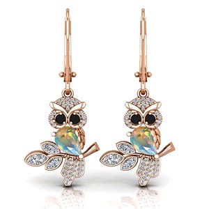 Könnte beinhalten: Ein Paar roségoldene Eulenohrringe. Jeder Ohrring hat ein Eulen-Design mit schwarzen Augen, einem birnenförmigen Opal und einem Zweig mit diamantartigen Akzenten. Die Ohrringe haben einen Klappbügelverschluss.