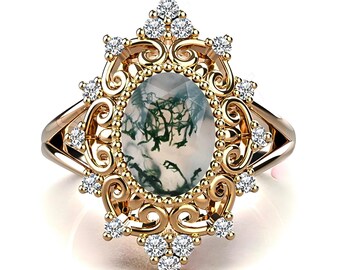 May include: A gold-toned ring featuring an oval moss agate gemstone with green inclusions. The ring is adorned with small, round diamonds and intricate filigree detailing, creating a vintage-inspired design. The ring's band has a split shank.