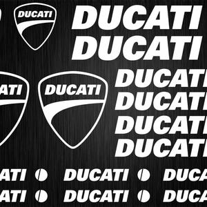 Pode incluir: Uma coleção de decalques Ducati brancos sobre um fundo preto. Os decalques incluem o logotipo da Ducati, um escudo com a palavra "DUCATI" e uma faixa branca, e a palavra "DUCATI" em uma fonte em negrito sem serifa.