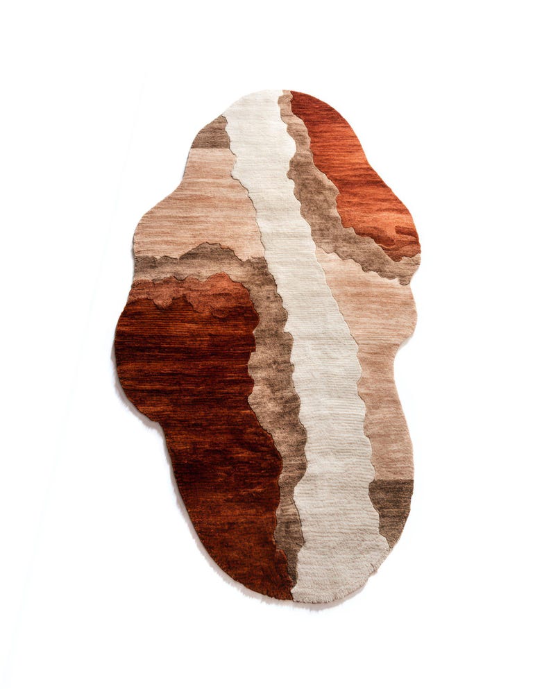 A vertically oriented irregular-shaped rug with wavy sections of dark brown, light brown, beige, and terracotta colors.