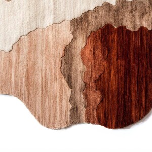 A close-up of the bottom edge of the irregular rug, showing wavy sections of dark brown, light brown, and beige.