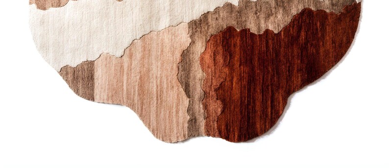 A close-up of the bottom edge of the irregular rug, showing wavy sections of dark brown, light brown, and beige.