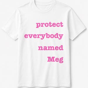 May include: White t-shirt with the pink text "protect everybody named Meg". The shirt has a crew neck and short sleeves. The text is centered on the front of the shirt.