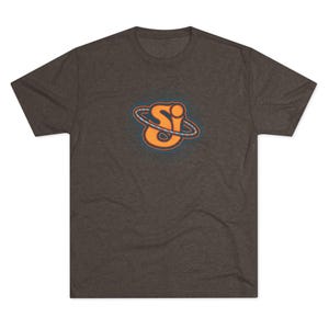 May include: Dark heather grey t-shirt with a retro-style orange and blue graphic of the letters "SI" inside a planet-like design. The short-sleeved shirt is made of a soft, comfortable material.