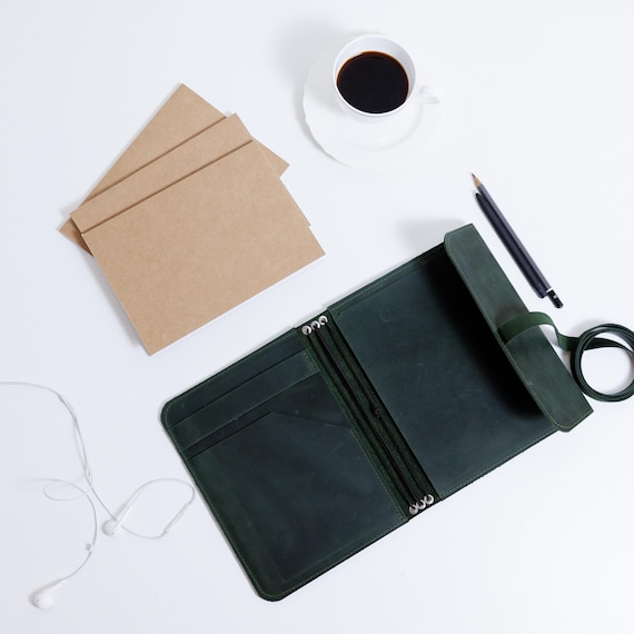 A hand-engraved leather notebook *cover* with elastic closure — a reusable, refillable craft object that feels genuinely made by hand, not just stamped.