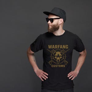 May include: Black t-shirt with a gold wolf graphic and the text "WARFANG CUSTOMS". The design features a wolf's head, crossed rifles, and a circular border. The shirt is made of a soft material.