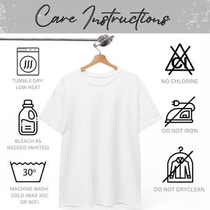 Puede incluir: Una camiseta blanca lisa colgada de una percha de madera. La imagen incluye instrucciones de cuidado: secar en secadora a baja temperatura, no usar lej&iacute;a, blanquear si es necesario, lavar a m&aacute;quina en fr&iacute;o (m&aacute;x. 30&deg;C), no planchar y no limpiar en seco.