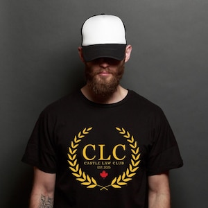 May include: Black t-shirt featuring a gold laurel wreath design with the text "CLC CASTLE LAW CLUB EST. 2025" and a red maple leaf. The person is wearing a black and white trucker hat.