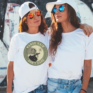 May include: Two people wearing white t-shirts, white caps, and sunglasses. The t-shirts have a circular graphic with the text "RANGE HAIR DON'T CARE" and an illustration of a person aiming a rifle. The sunglasses have round frames.