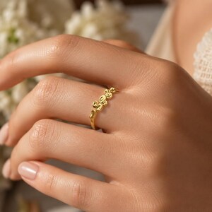 Könnte beinhalten: Ein goldener Ring mit einem Band, das mit einer Reihe kleiner, erhabener, organischer, kieselartiger kreisförmiger Formen verziert ist. Das Metall hat eine polierte, reflektierende Oberfläche, die ein strukturiertes Aussehen erzeugt.