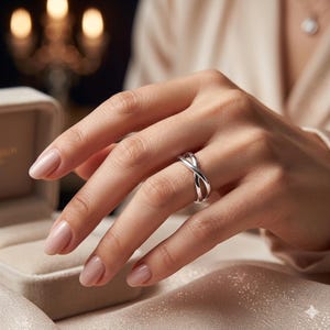 Può includere: Un anello in argento lucido caratterizzato da un design incrociato con due fasce che si intersecano formando una figura simile all'infinito. L'anello presenta una finitura metallica liscia e riflettente, indossato al dito con eleganza.