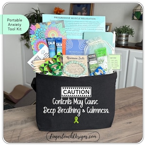 May include: A black tote bag labeled "Portable Anxiety Tool Kit" filled with relaxation aids. Contents include "CALM" lotion, a Burmese Jade bracelet, and a booklet on progressive muscle relaxation. The bag has a "CAUTION" label with the text "Contents May Cause Deep Breathing & Calmness."