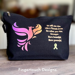 May include: Black zippered cosmetic bag with a phoenix design in shades of pink and orange. The bag features inspirational text and a yellow ribbon. The text reads "Yet still you rise. Like a Phoenix from the ashes you rise. Stronger. More beautiful. More powerful."