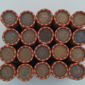 May include: A collection of rolled Indian Head pennies, each wrapped in a paper tube with orange and white stripes. The coins are a mix of brown and copper tones, with the profile of a Native American on each coin.
