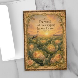 May include: A greeting card with a vintage illustration of a cabbage field with babies nestled inside. The card has the text "The world had been keeping this one for you." A white envelope, black pen, and black glasses are also in the image.