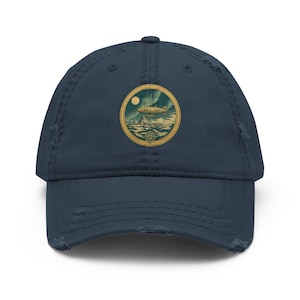 May include: Navy blue distressed baseball cap with a circular patch featuring a vintage airship design. The patch includes a moon, water, and a compass. The cap has a pre-curved visor and distressed detailing.