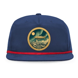 May include: Navy blue baseball cap with a red rope detail. The cap features a circular patch with a vintage illustration of a zeppelin, mountains, and a compass. The design is set against a backdrop of an aurora borealis and a full moon.