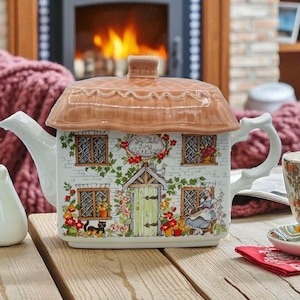 Può includere: Teiera decorativa a forma di cottage, con tetto di paglia marrone e facciata in mattoni bianchi. La teiera presenta un motivo floreale con la scritta "Ye Olde Ivy Cottage" e un gatto nero. Il manico e il beccuccio sono bianchi.