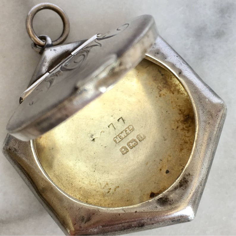 May include: Silver locket with an engraved design on the lid. The locket is open, revealing a blank interior. The locket is marked with the inscription "925" and "C 717".