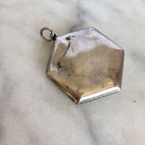 May include: A silver hexagonal locket pendant with a loop for attaching a chain.