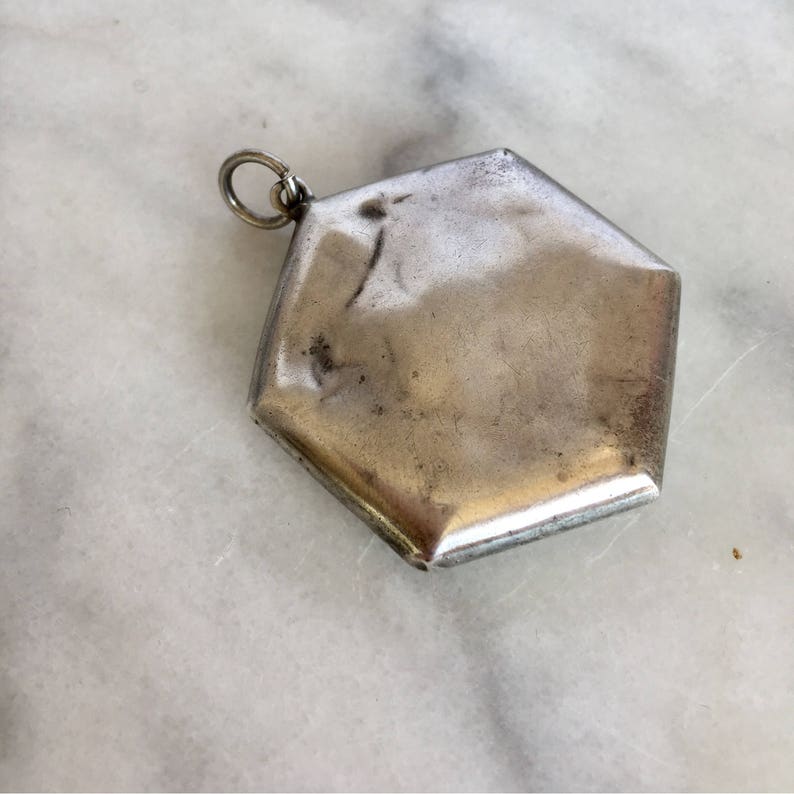 May include: A silver hexagonal locket pendant with a loop for attaching a chain.