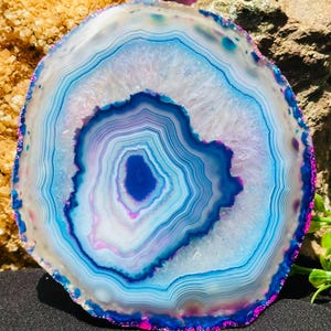 Könnte beinhalten: Eine kreisförmige Achat-Scheibe mit konzentrischen Bändern in Blau, Weiß und Violett. Die Mitte zeigt einen tiefblauen Kern, umgeben von durchscheinenden weißen und hellblauen Schichten, mit einem lebhaft texturierten äußeren Rand.